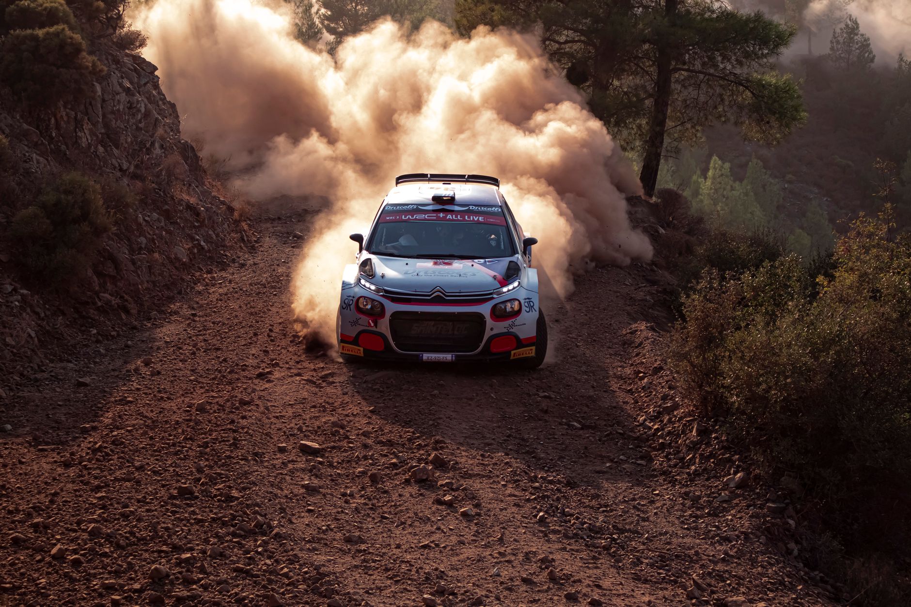 A sports car races down a dusty dirt road, showcasing speed and endurance in a rugged environment.