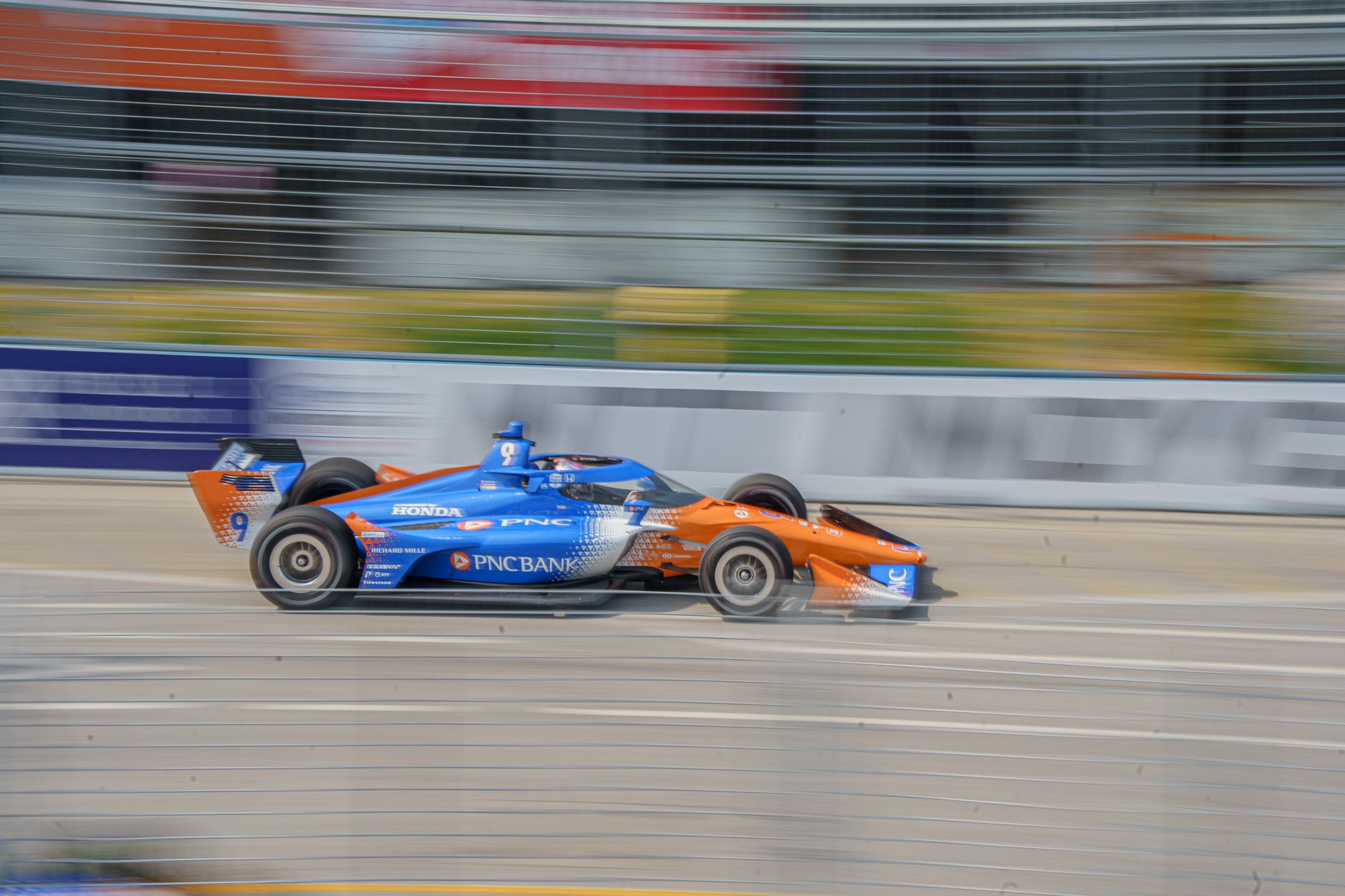 Orange and blue race car zooming on Toronto track, showcasing vibrant motion and racing dynamics.