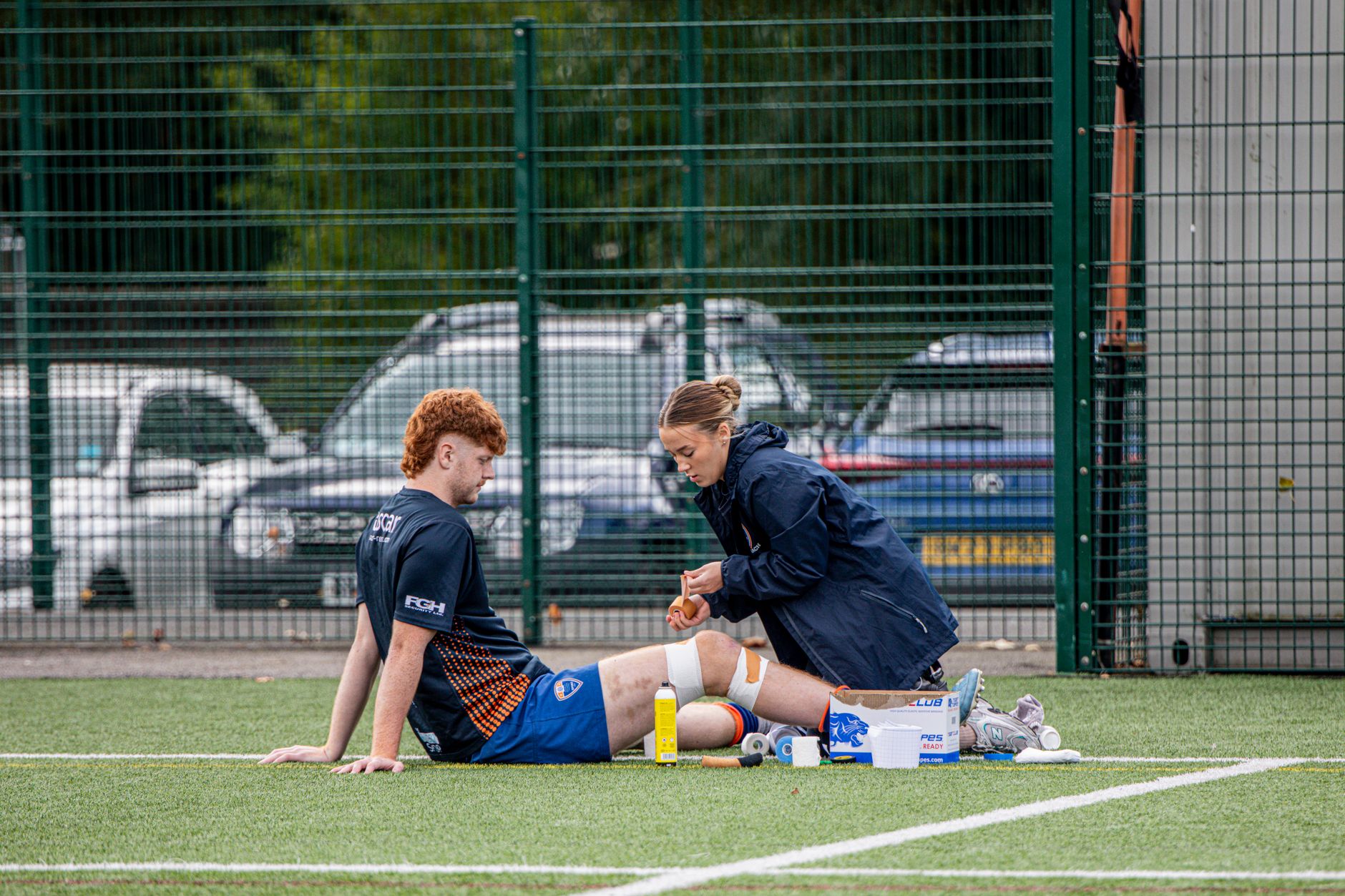 A sports therapist tends to an injured athlete on an outdoor football field.