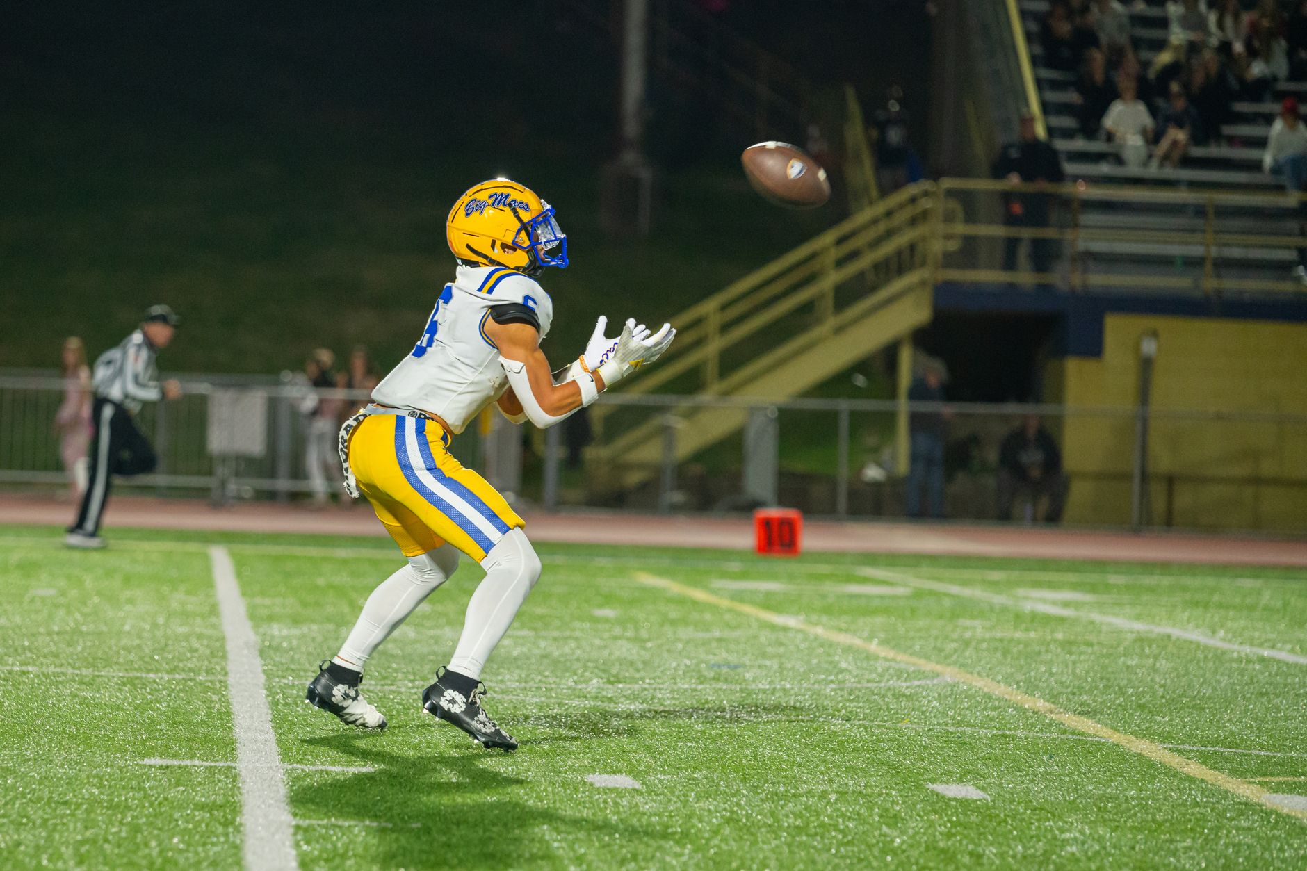 A high school football player wearing full gear catches a pass during an evening game on the field.
