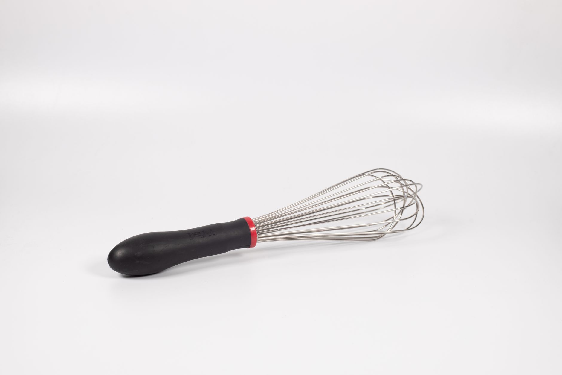 Close-up of a stainless steel kitchen whisk with black handle, isolated on a white background.