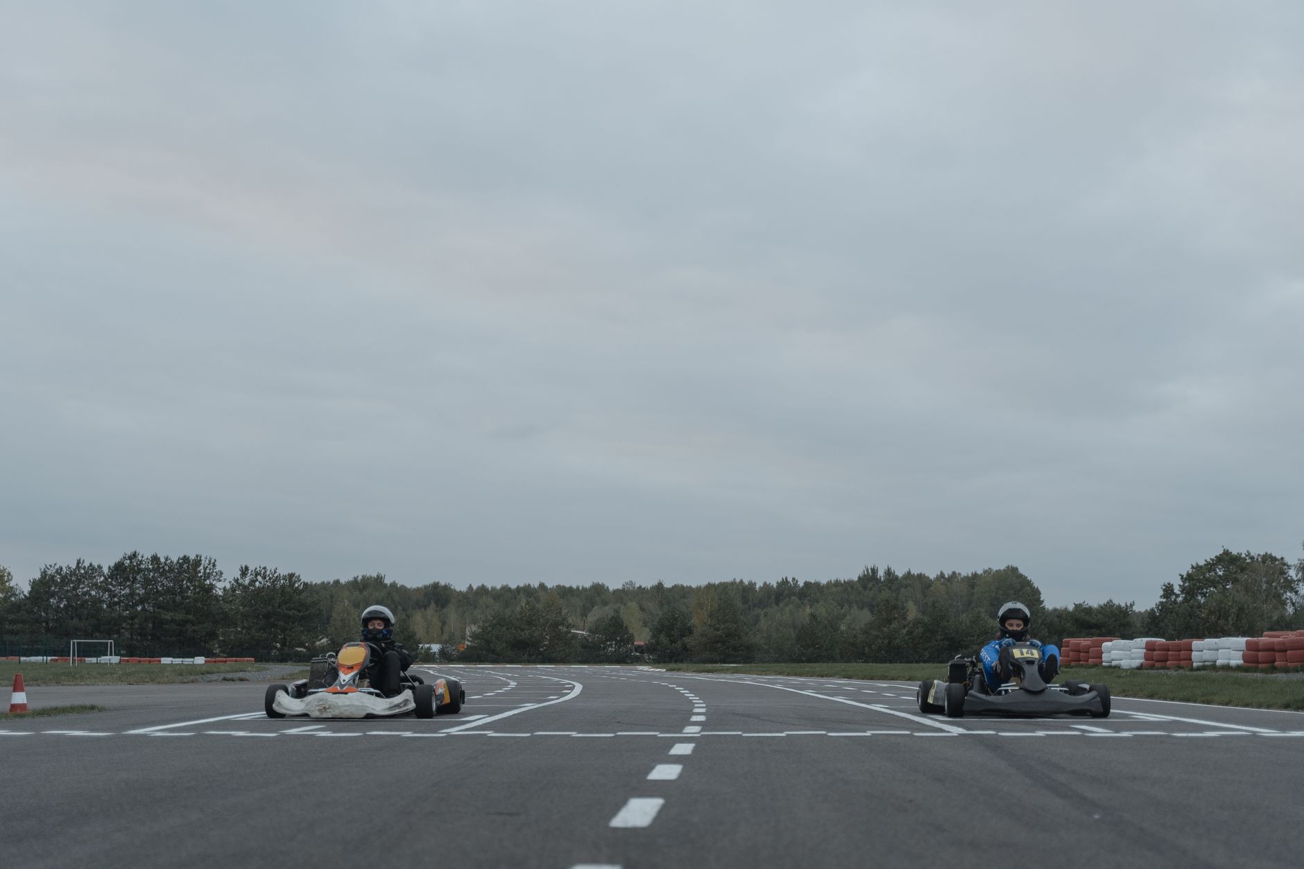 Two athletes racing go-karts on an outdoor racetrack in overcast conditions.