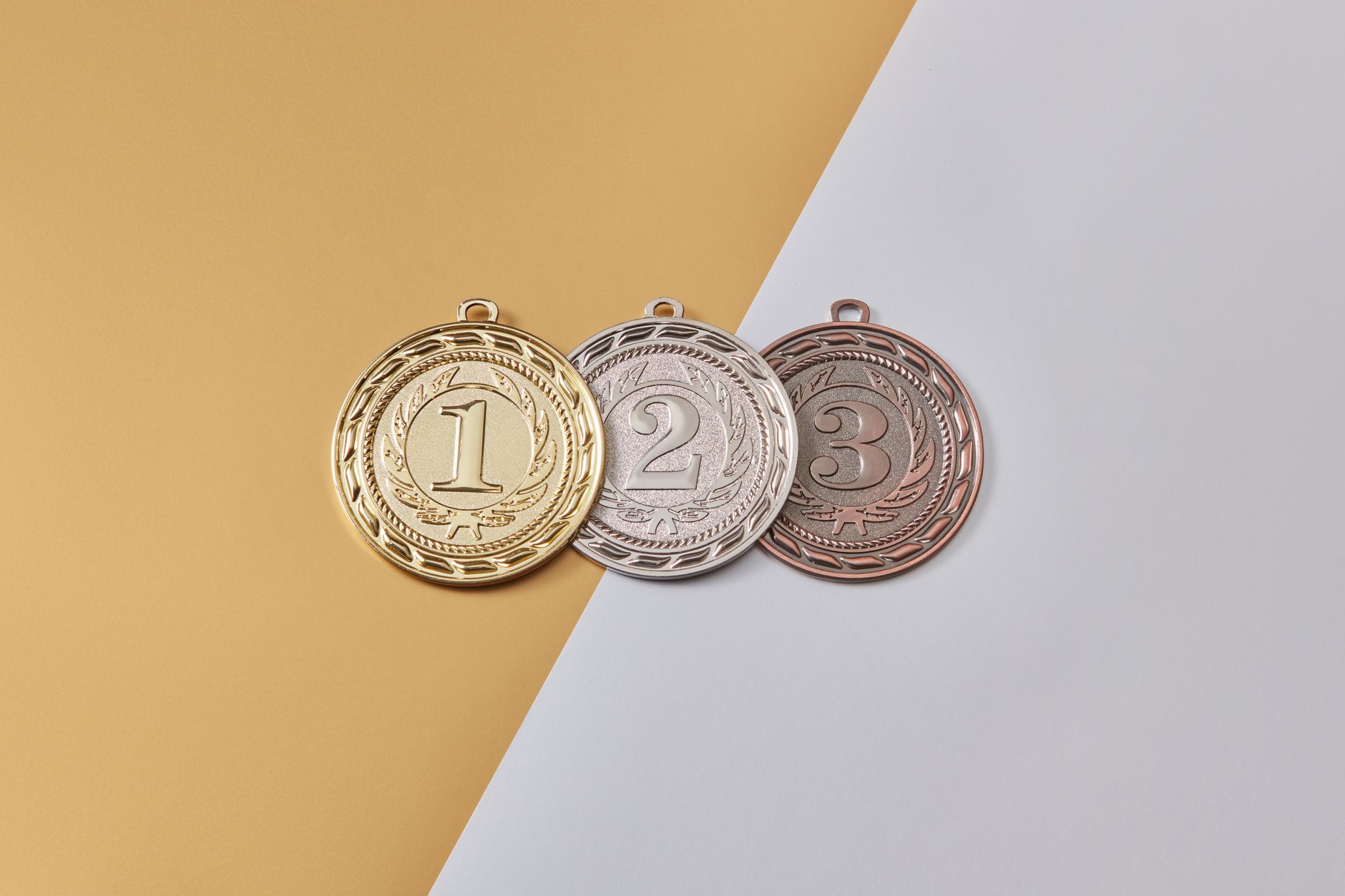 Gold, silver, and bronze medals placed on a modern split-color background, symbolizing achievement.