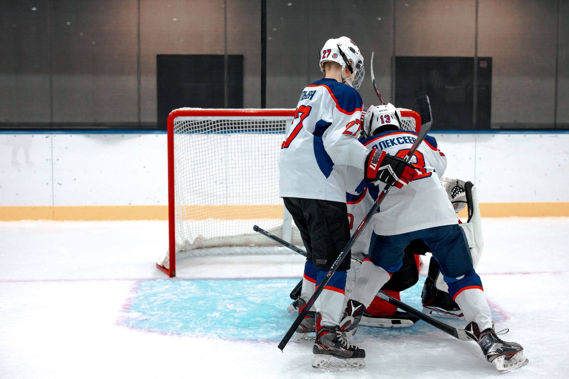 Ice hockey players compete intensely near the goal on a rink.