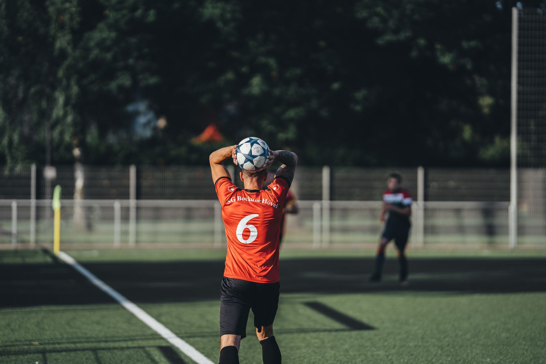 Focused soccer player in red jersey preparing to throw the ball during a match on a sunny day.