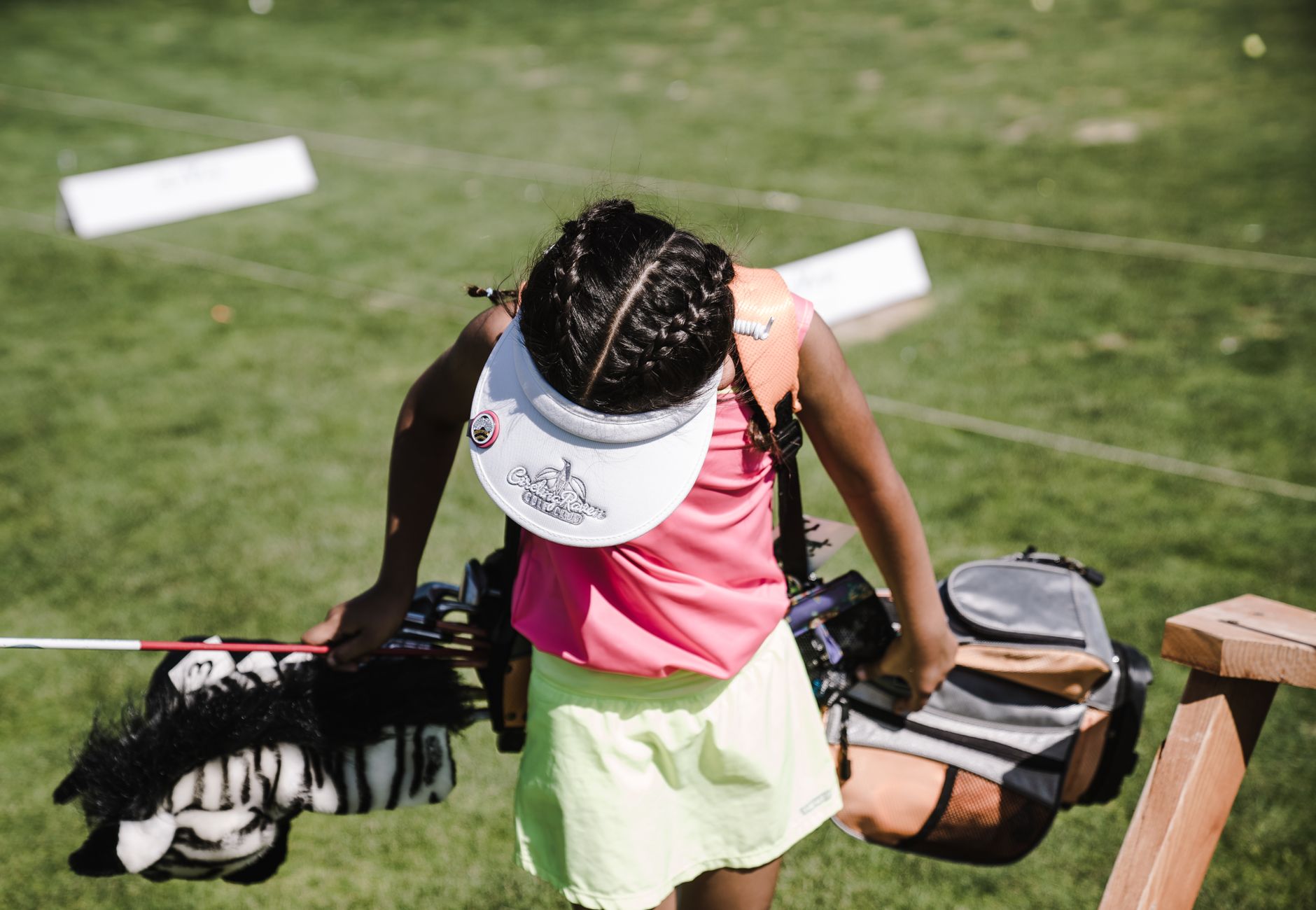 A young girl in vibrant sportswear practices her golf swing outdoors on a sunny day.
